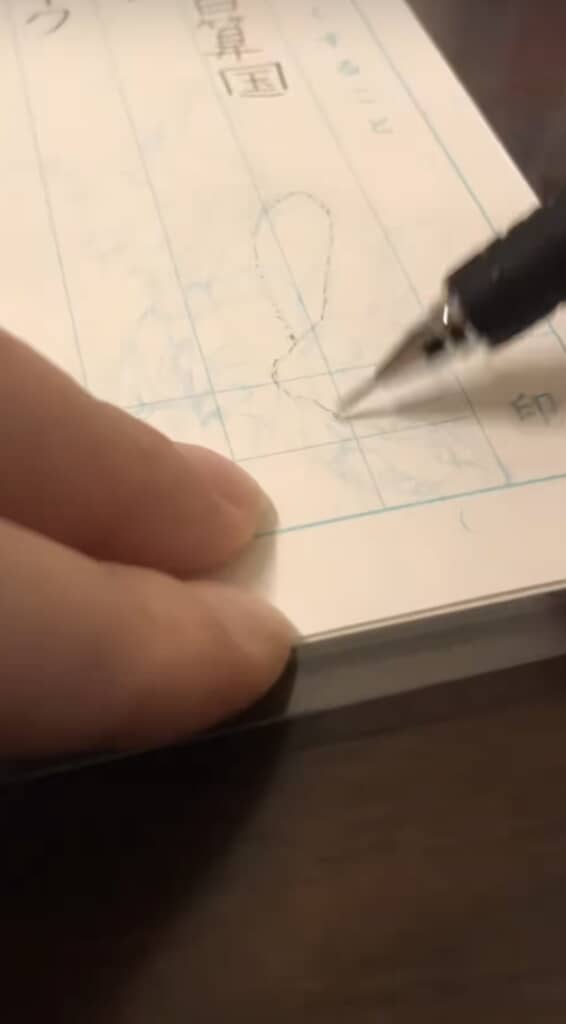 ノートに下書き線をなぞるペン先のアップ