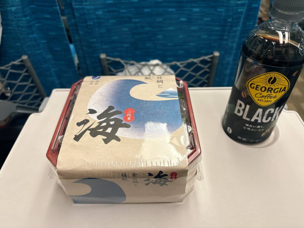 包装された駅弁とボトル入りブラックコーヒー