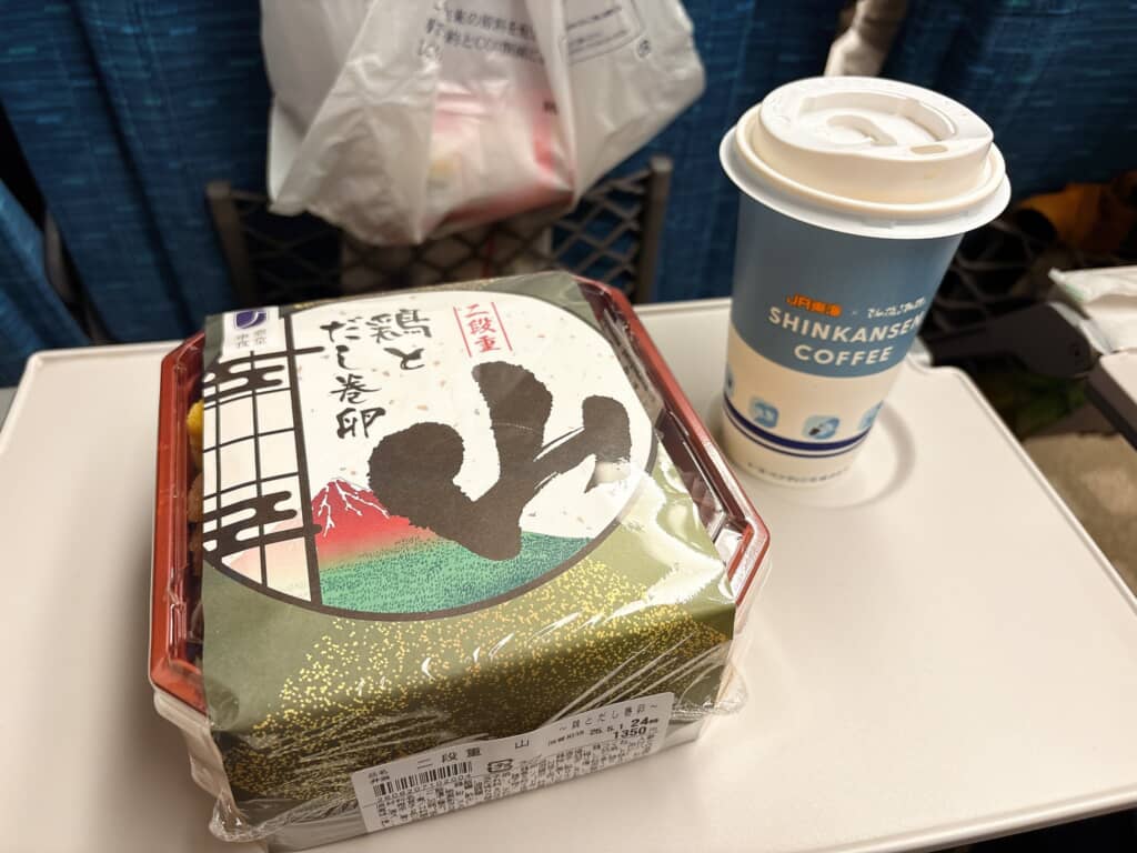 新幹線のテーブルに駅弁と紙カップコーヒー