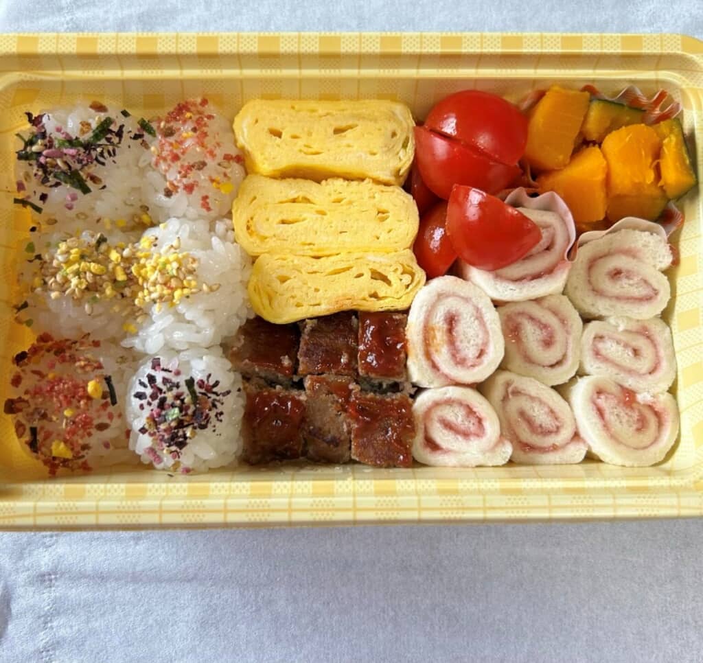 小さな丸いおにぎりとくるくると巻いたサンドイッチが美味しそうなお弁当