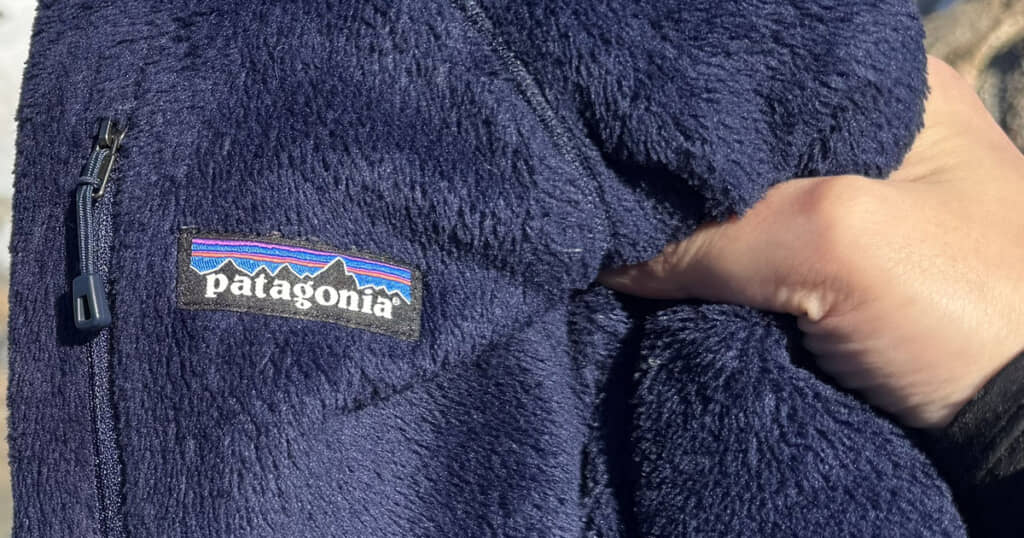 パタゴニアのロゴが付いた紺色のフリース素材を指で押さえている様子
