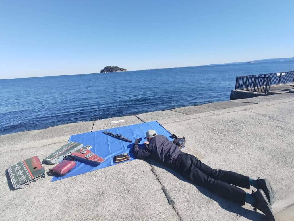 船の模型を撮るため地面に寝そべっている投稿者