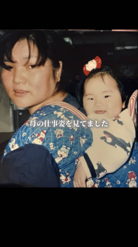 働く母の背中で笑顔を見せる娘さん