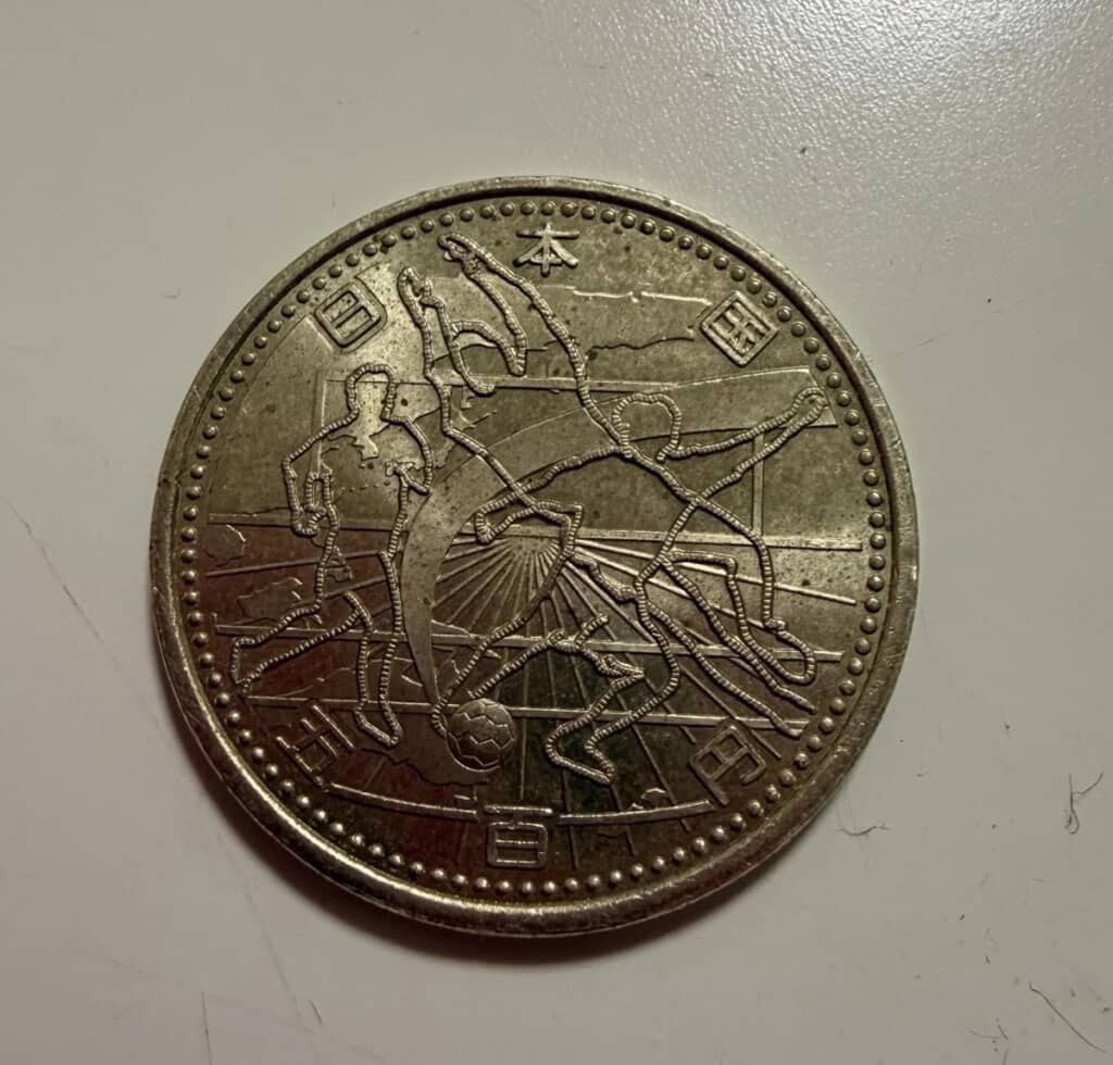 選手と地図の図柄が刻まれている「2002FIFAワールドカップ記念500円ニッケル黄銅貨幣」の表面
