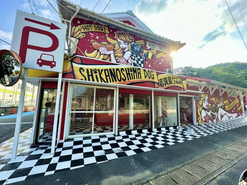 ホットドッグを持っている女性と犬の絵が描かれている志賀島ドッグ2号店の外観