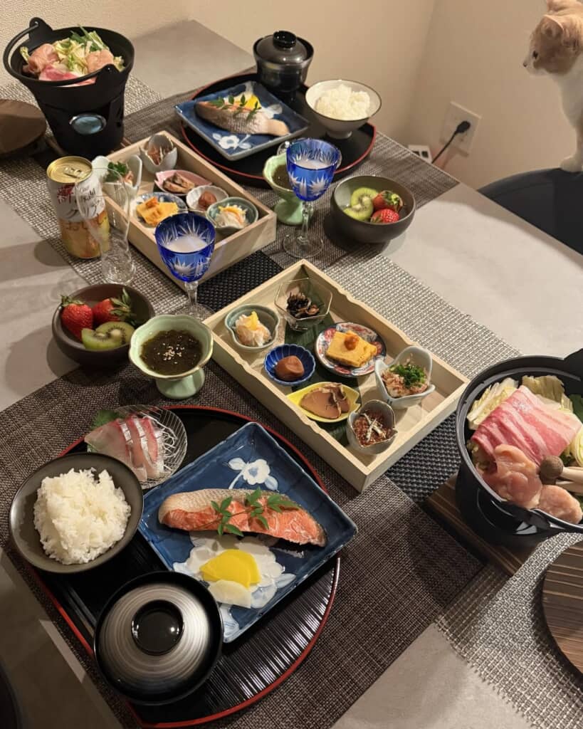 猫が側で見守る、小鍋や焼き魚、多彩な副菜が並ぶ豪華な二人分の和食膳