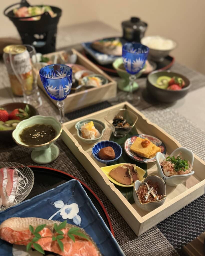 木箱に盛り付けられた多彩な副菜と焼き魚、刺身が並ぶ和食の食卓
