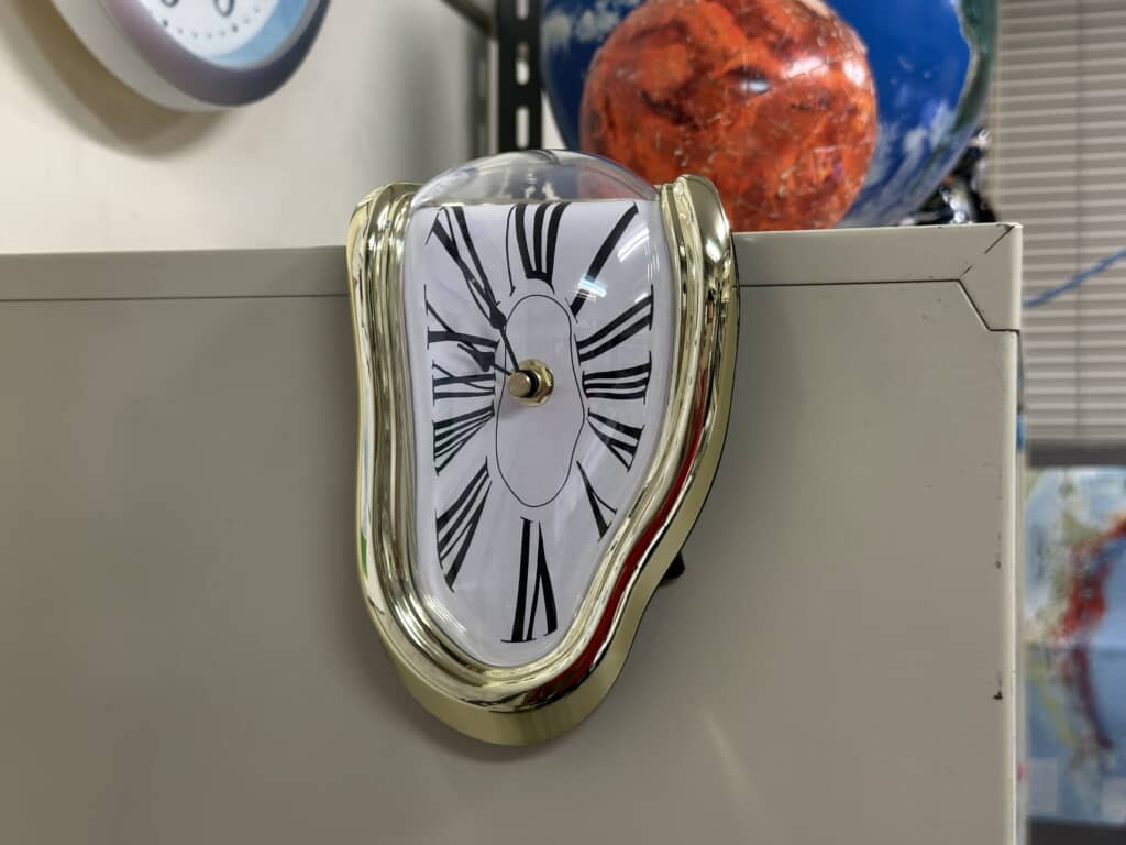 棚の角に掛かるダリの絵画風の溶けたデザインの置時計