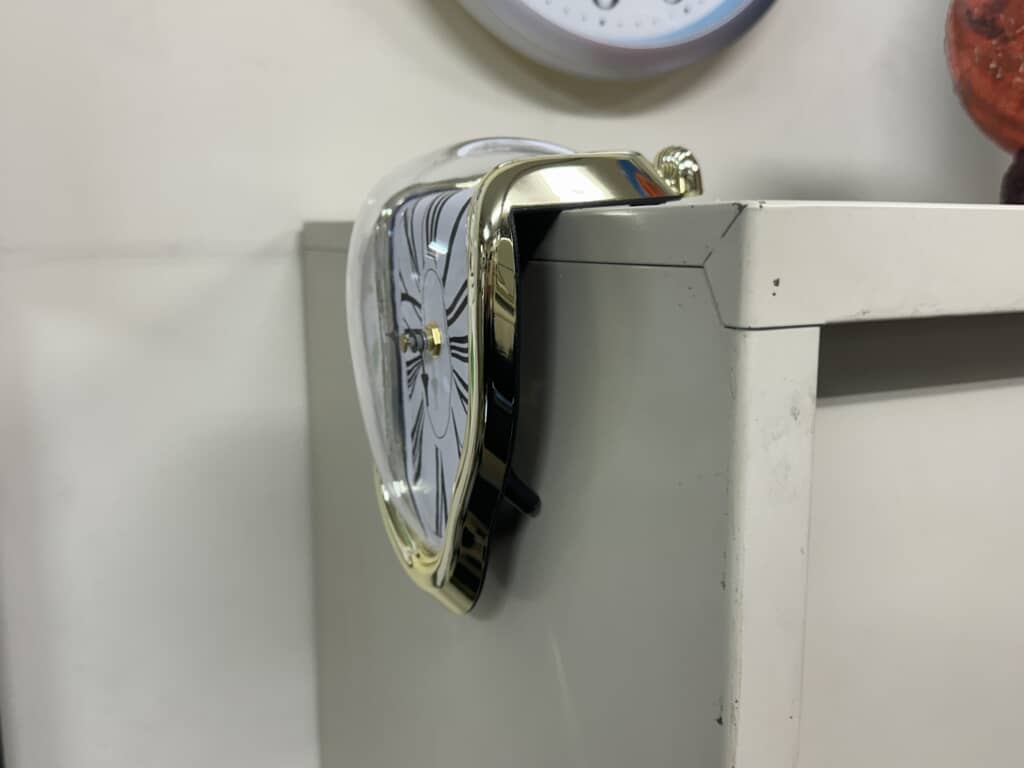 棚の角にフィットするように曲がった金色の縁の溶けた時計を横から見た様子