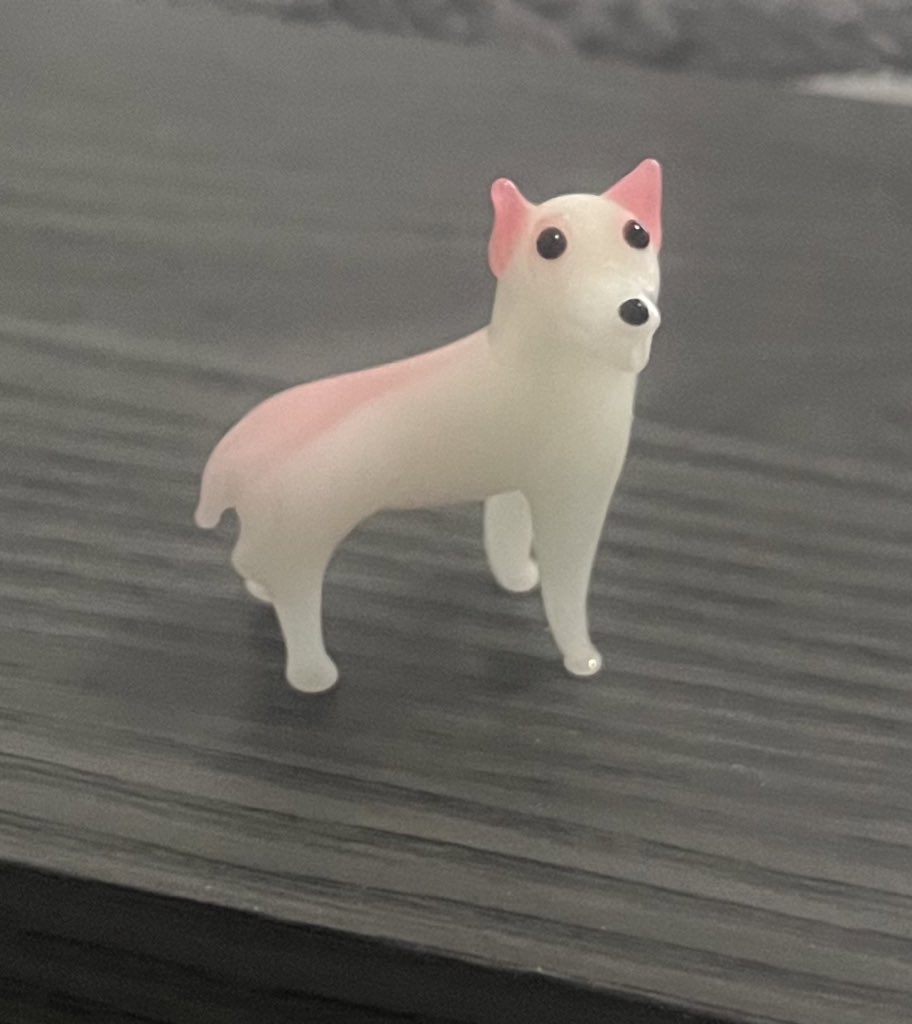 黒いテーブルの上に置かれた、耳と背中がピンク色の白い犬の置物
