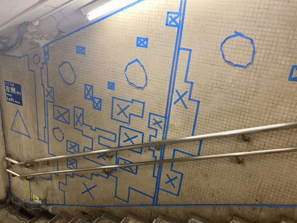 青いテープで壁面に形作られた丸印や三角印、四角に区切られたエリアの中の×印