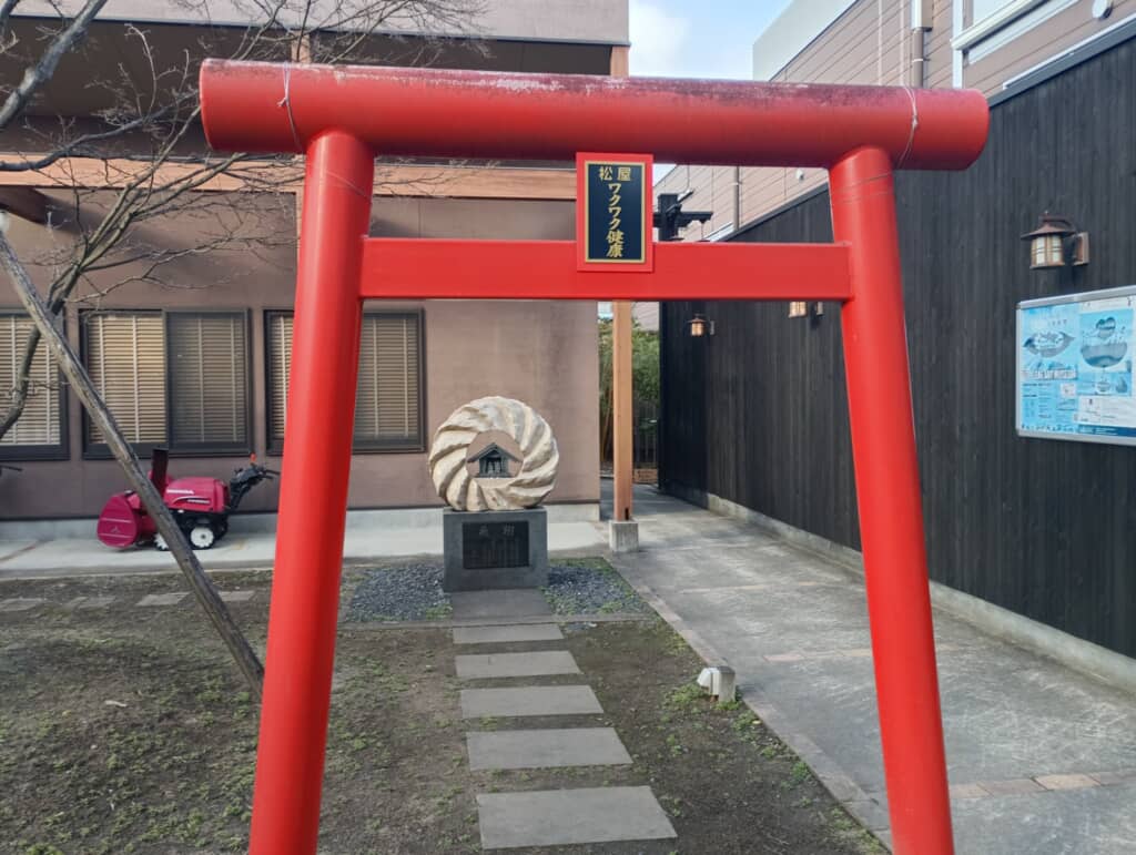 松屋ワクワク健康の看板がある赤い鳥居とフレンチクルーラーの石碑