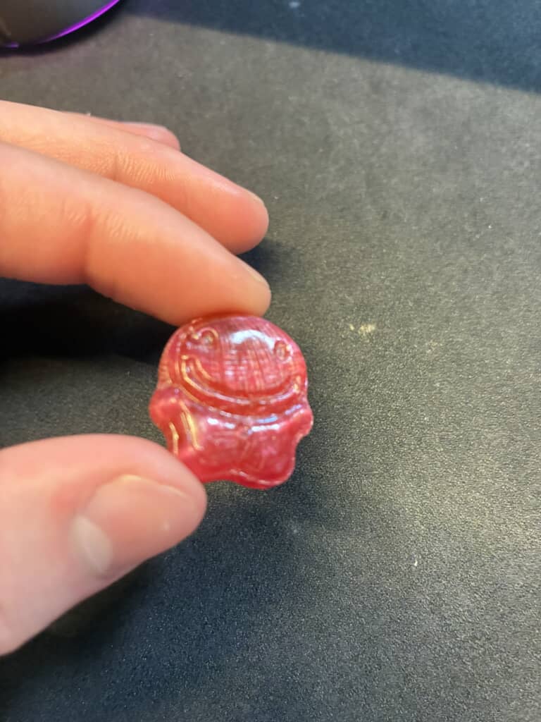 指先でつまんだ赤色の笑顔の形をした飴
