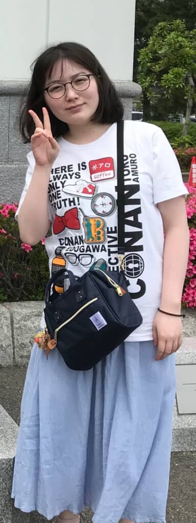 ボブヘアでメガネをかけた女性がカメラに向かってピースサインをしている