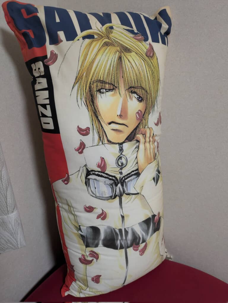 『最遊記』のキャラクター「玄奘三蔵」が描かれたロングピロー。金髪で不機嫌そうな表情の三蔵と、舞い散る花びらがデザインされている。