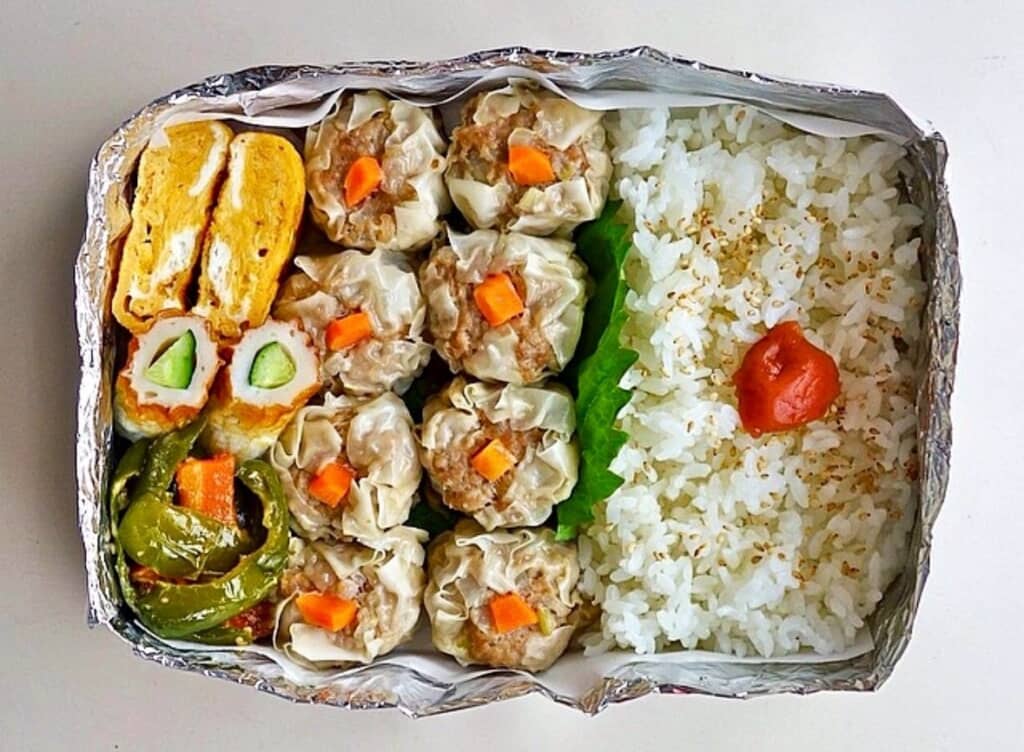 アルミホイル製の容器に詰めた白飯や卵焼き、シューマイ、ちくわキュウリ