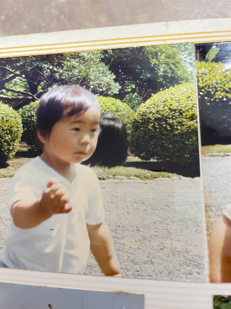 屋外にいる幼い少年とその顔の隣に写っている黒いもの