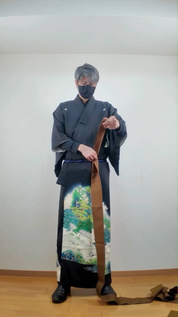 男性用の着物の帯を巻く