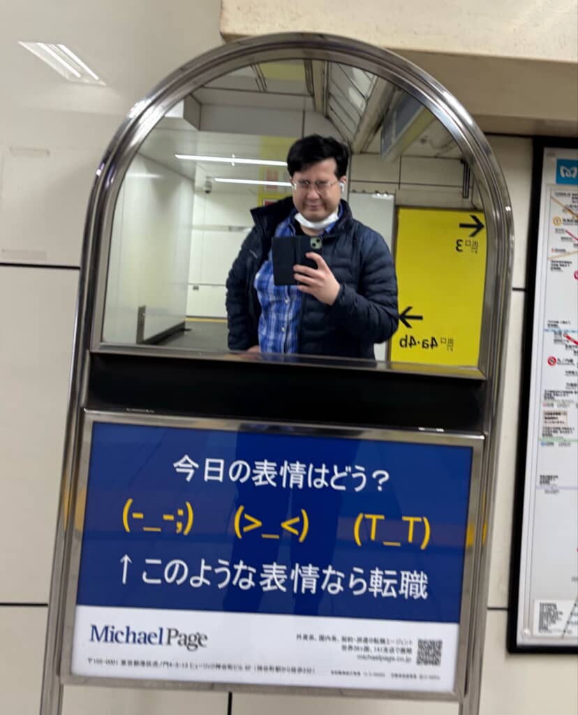 駅の鏡で自撮りする男性と転職広告