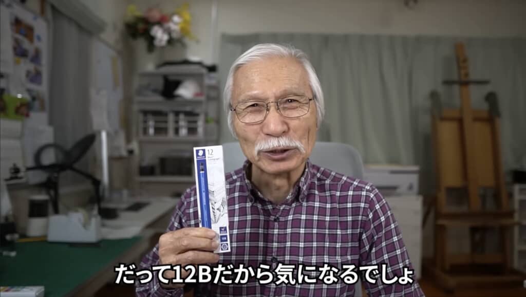 12Bの鉛筆のパッケージを手に持ち微笑む白髪の男性