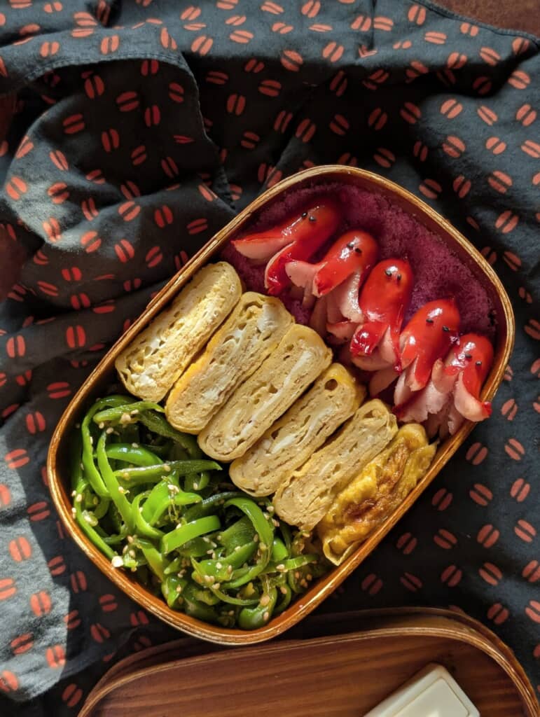 木製弁当箱に斜めに配置された厚焼き玉子、ピーマンの胡麻和え、タコさんウインナー