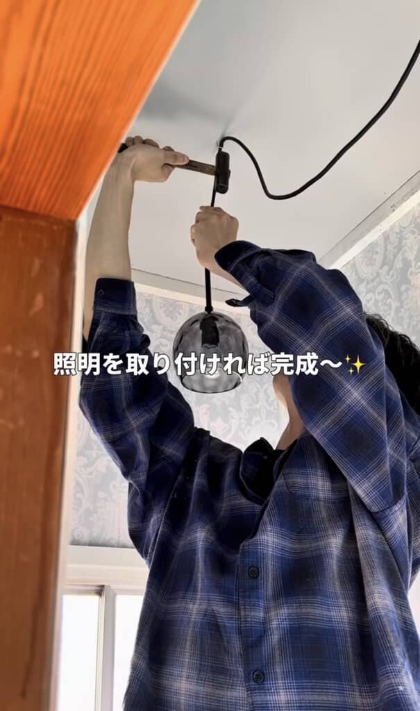 天井に黒いペンダントライトの照明を取り付ける男性