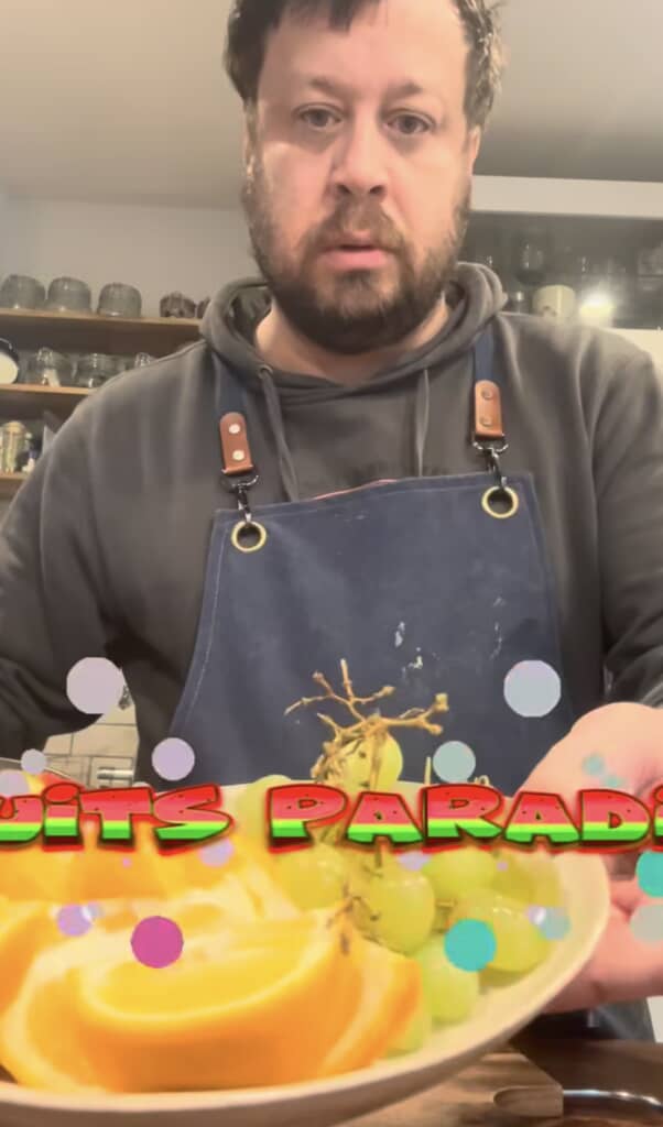 オレンジスライスとマスカットが盛られたフルーツプレートを持つ男性。テロップ「FRUITS PARADISE」
