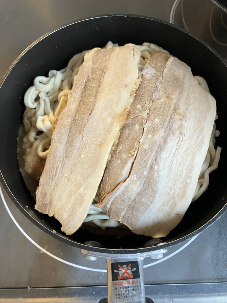 フライパンで煮込み中の濃厚G系ラーメン・太麺にチャーシューをのせた調理工程
