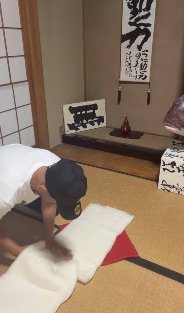 白い綿素材を畳の上で広げ作業する男性の様子