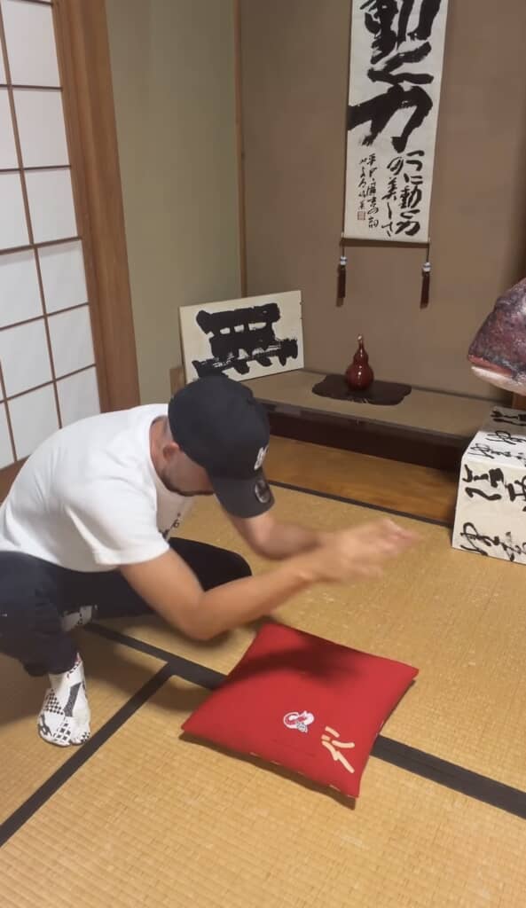 和室の畳でかっぱえびせんデザインの赤いクッションを叩く男性
