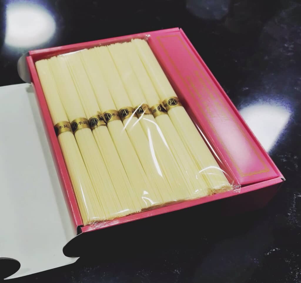 箱に入った島原手延そうめんと「株主優待 島原素麺」と書かれたピンク色のパッケージ