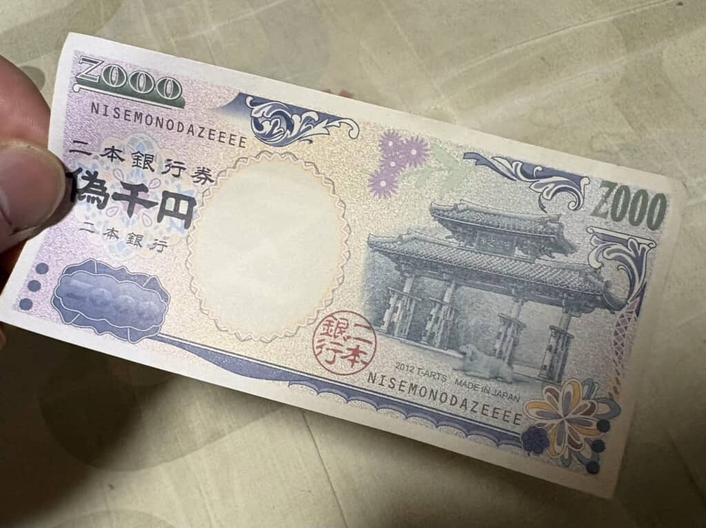 「偽千円」と書かれたおもちゃの紙幣を手に持つ様子
