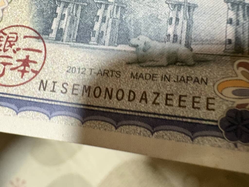 偽千円札風おもちゃの「NISEMONODAZEEEE」表記を接写した様子