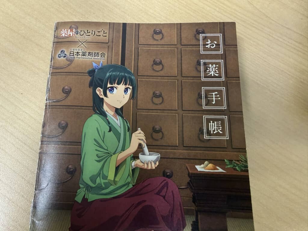 薬屋のひとりごと×日本薬剤師会コラボのお薬手帳表紙（猫猫がすり鉢で薬を調合するイラスト）