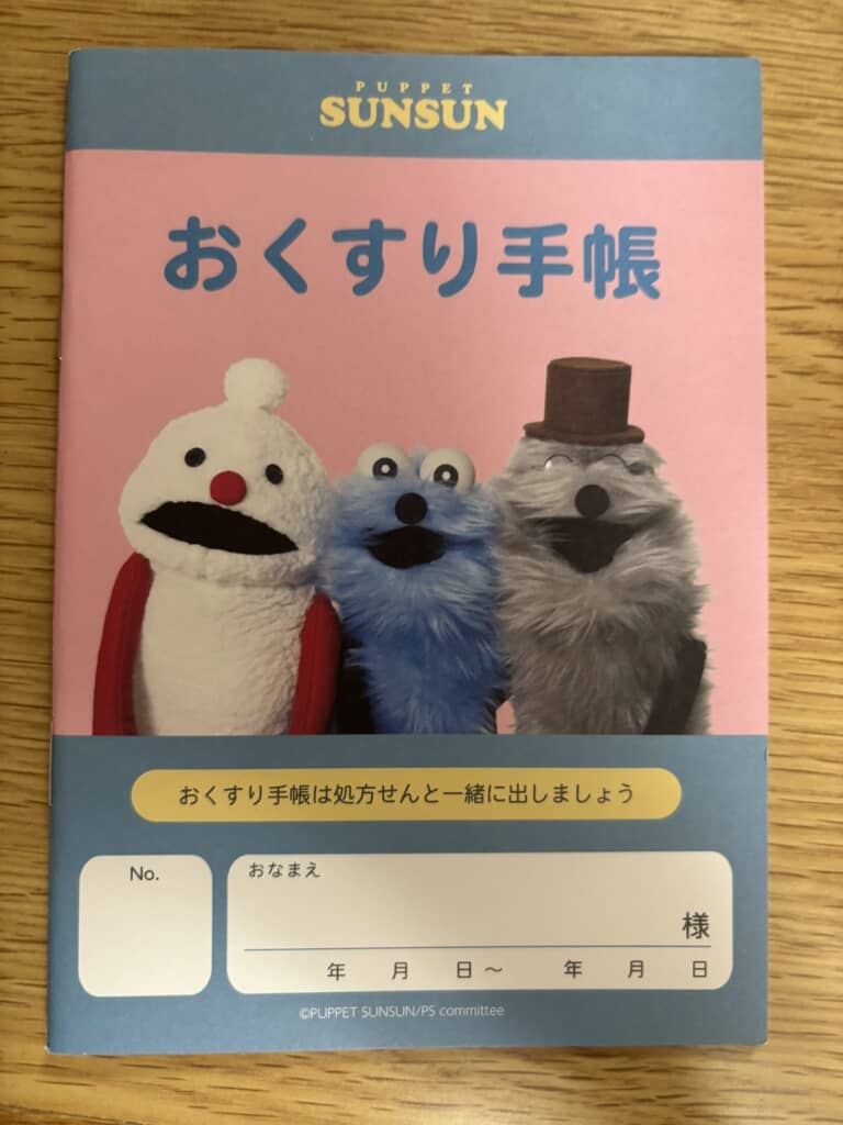 PUPPET SUNSUNのキャラクター3体が並ぶおくすり手帳の表紙
