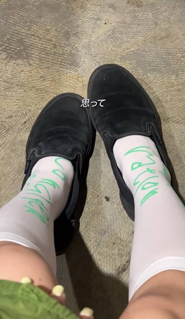 黒いローファーと「思って」の字幕が入った白いロゴ入り靴下のコーデ