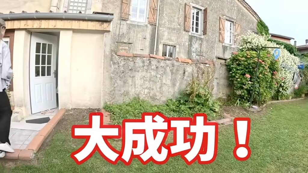 フランスの民家の庭先で「大成功!」の文字とともに立つ人物、成功を伝える演出