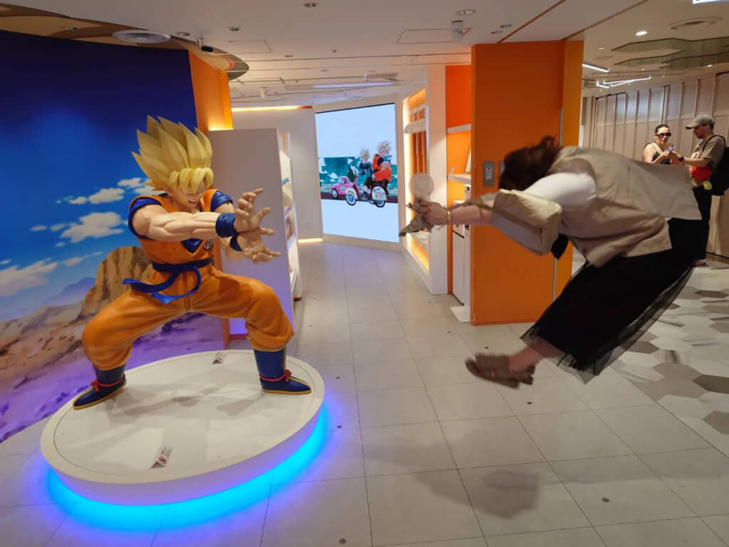 かめはめ波を放つ立像の前で、体をくの字にしてジャンプしている人