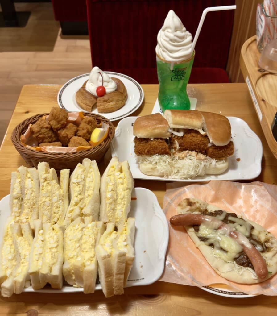 店内で楽しむエビカツバーガーや卵サンド、フライドチキン、メロンソーダフロートなどの豪華な食事風景