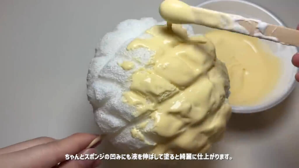 メロンパンにパンの生地っぽい色のコーティング液を塗っていく様子