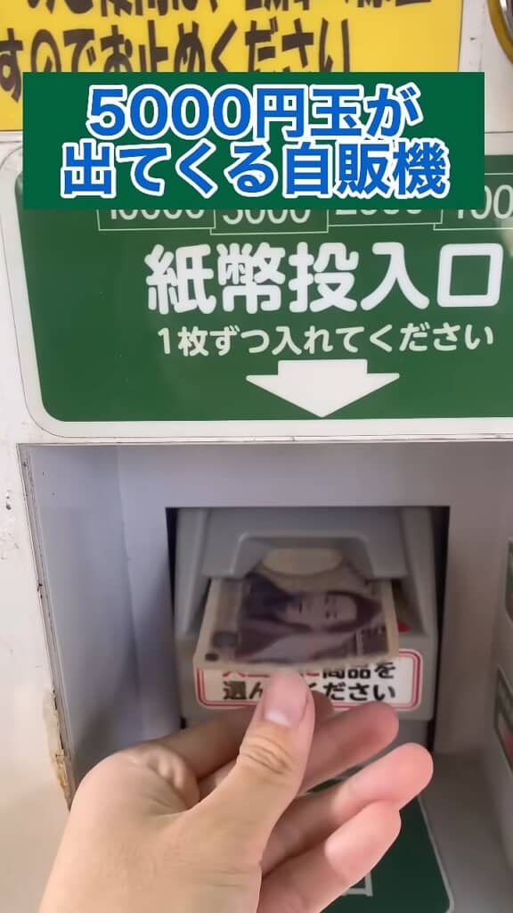 5000円玉が出てくる自販機の紙幣投入口に5000円札を挿入する手元