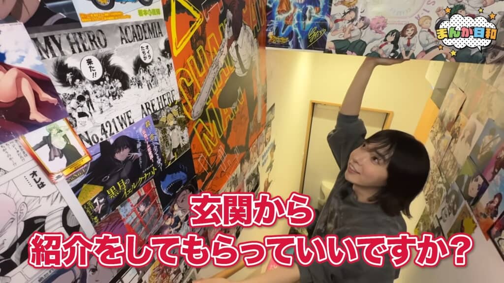 玄関の壁一面に貼られたアニメポスターと、玄関を案内するハヤン君