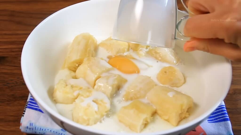 白いボウルに潰したバナナと卵、牛乳を注ぐ手元