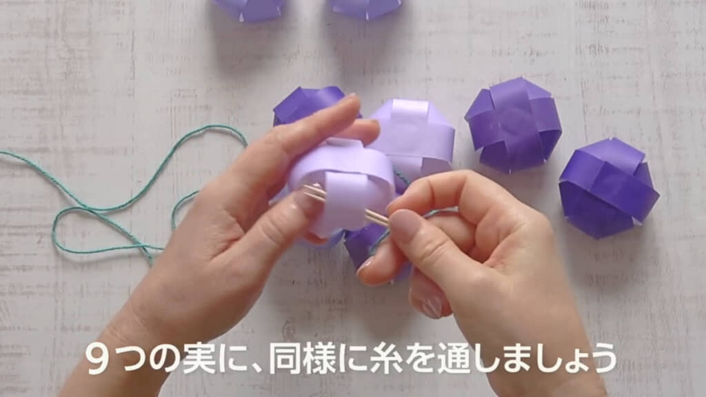 9つの実に糸を通します。折り紙は濃い紫色~薄い紫色と少しグラデーションを持たせています