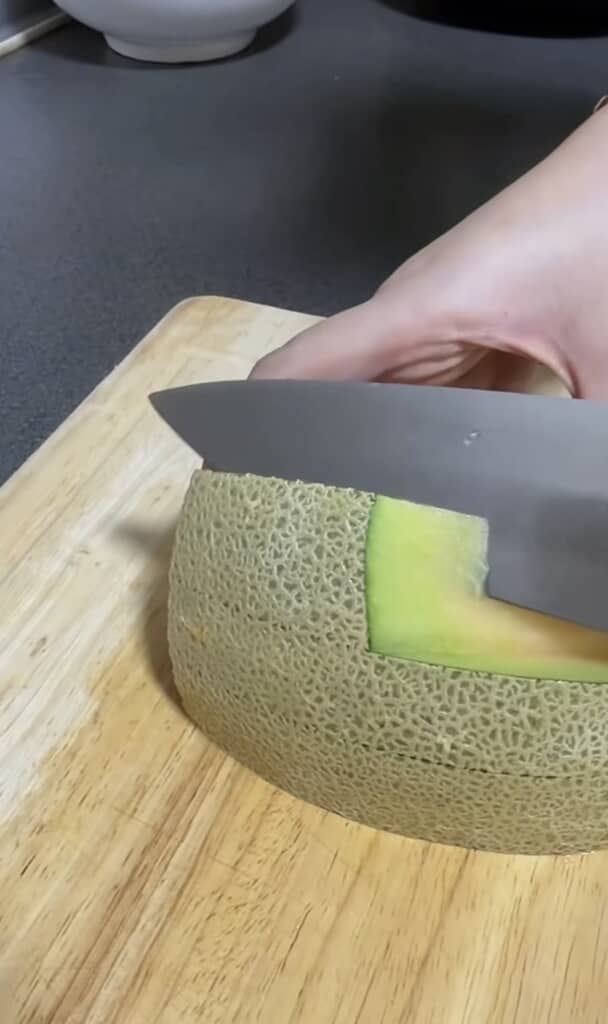 半月切りにしたメロンの果肉と皮の間に包丁を入れて切り離す様子