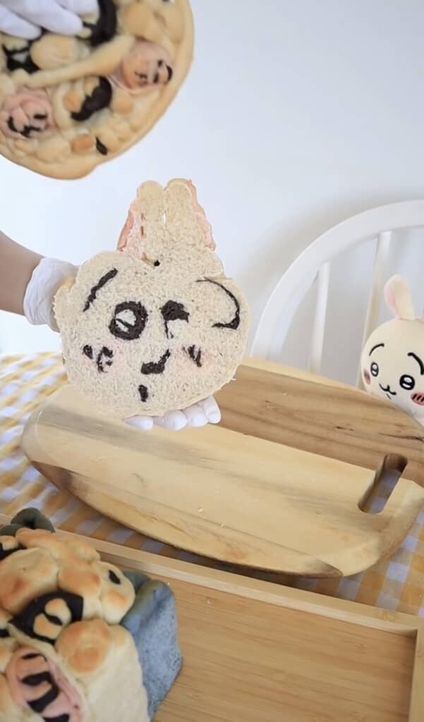 うさぎ風キャラクターの顔を描いた丸い食パンを手に持つ様子