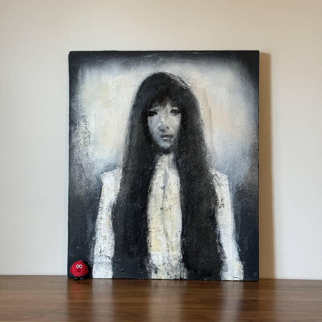 長い黒髪の女性をモノクロ調で描いた人物画と赤い小さなオブジェ