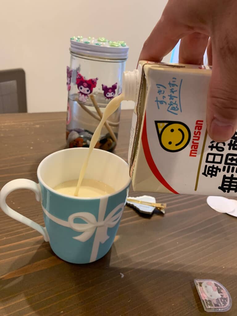注ぎ口を上側にしてキャップ付き紙パックの豆乳をコップに注ぐ様子