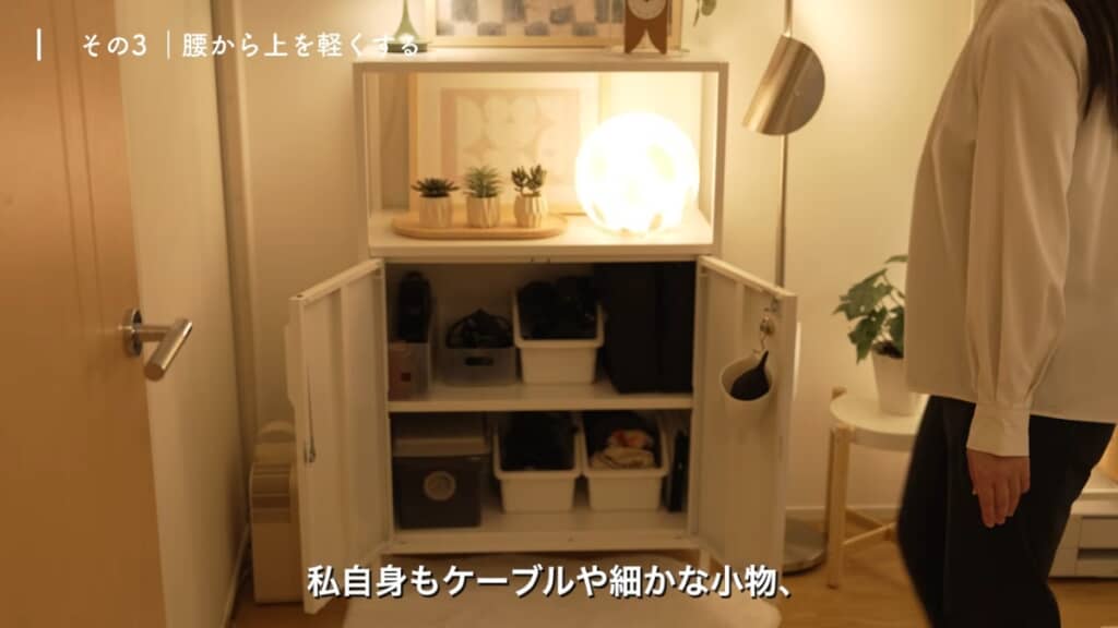 収納の隣に立って腰の高さと比べている。ケーブルや細かな小物、撮影機材は中が見えない箱型キャビネットに