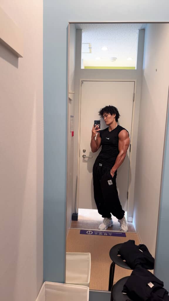 鏡の前で黒いトレーニングウェア姿を撮影する筋肉質な男性